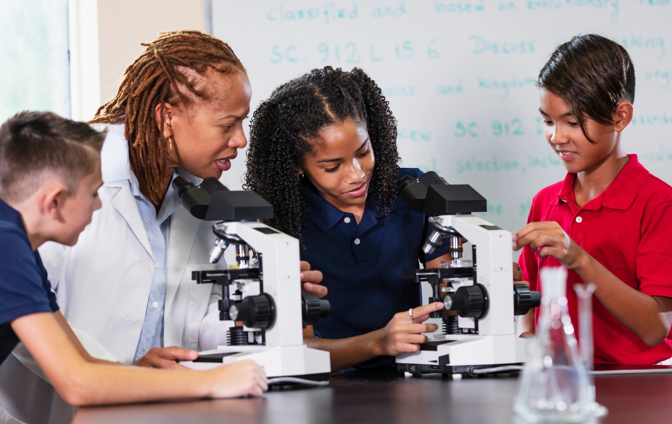 Grupo de estudiantes usando microscopios en laboratorio escolar